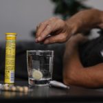Elderly man lays in bed while dissolving a soluble medicine in water, indicating health and wellness home care.